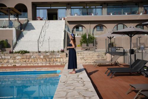 a woman is standing next to a swimming pool at Iolida Corfu Resort & Spa by Smile Hotels in Dassia