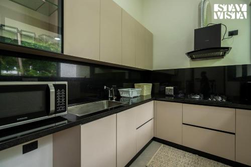 a kitchen with white cabinets and a sink and a microwave at StayVista at M Villa with Breakfast Included in Bengaluru