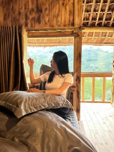 a woman sitting on a bed looking out a window at Tay Eco House in Ha Giang