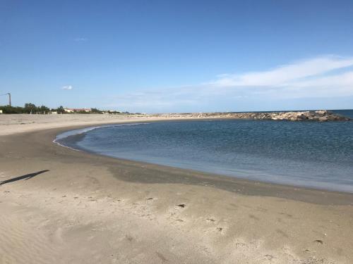 une plage de sable avec de l'eau et des rochers en arrière-plan dans l'établissement Appartement à 20 m de la plage, à Frontignan