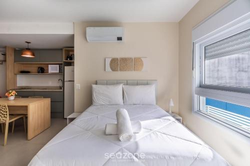 a bedroom with a white bed with a desk and a window at Studio encantador e bem localizado PoA-RS VENB504 in Partenon