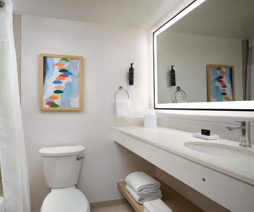 a white bathroom with a sink and a mirror at The Ellie Beach Resort Myrtle Beach, Tapestry By Hilton in Myrtle Beach