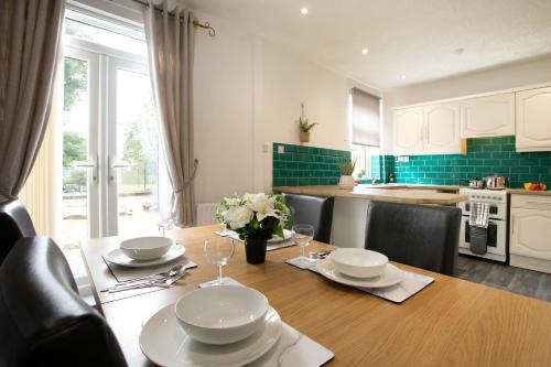 a kitchen with a wooden table with plates and wine glasses at Manvers House, Rotherham for contractors, Families, free parking, Spacious, WIFI, modern in Wath upon Dearne
