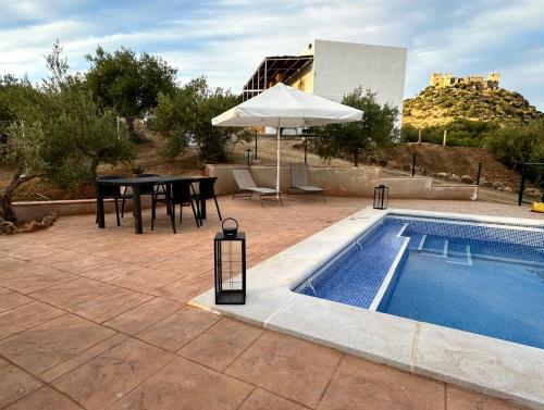 a patio with a table and an umbrella next to a pool at Casa Caraza. Un olivar con vistas al castillo de Juego de Tronos in Almodóvar del Río