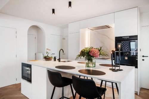 a kitchen with a large white island with black chairs at Sejoylia Knokke: app 2ch luxueux au centre de KH in Knokke-Heist