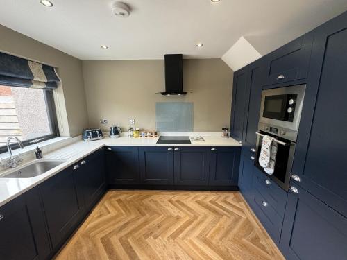 a kitchen with navy blue cabinets and a wooden floor at Victoria Cottage, Cullercoats in Cullercoats