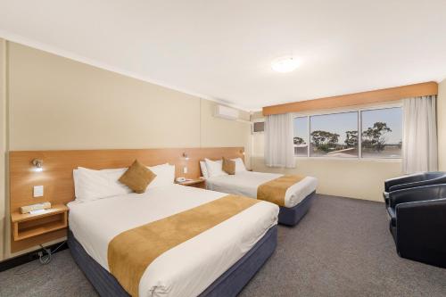a hotel room with two beds and a chair at Ciloms Airport Lodge Melbourne Airport in Melbourne
