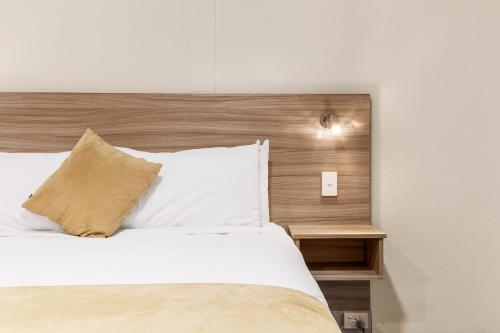 a bedroom with a white bed with a wooden headboard at Ciloms Airport Lodge Melbourne Airport in Melbourne
