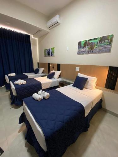 a hotel room with three beds with blue sheets at Visionsul Hotel in Chapadão do Sul