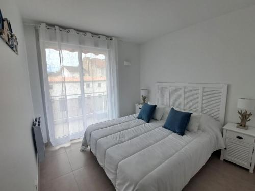 une chambre blanche avec un grand lit avec des oreillers bleus dans l'établissement L'Océanide, F2 plage du Bureau, vue mer latérale, à Saint-Palais-sur-Mer