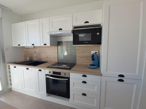 une cuisine avec des armoires blanches et des appareils noirs dans l'établissement L'Océanide, F2 plage du Bureau, vue mer latérale, à Saint-Palais-sur-Mer