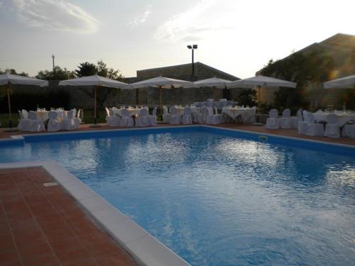 a swimming pool with white chairs and tables and umbrellas at AgriturismoBugilfezza di TGESD in Modica