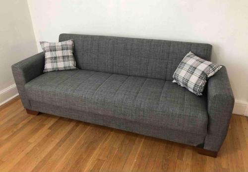 a gray couch with two pillows on a wooden floor at Spacious 2 bedroom apartment with 1 bathroom and private street entrance in Paterson