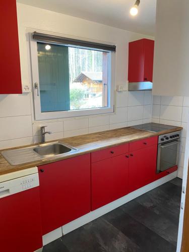 a kitchen with red cabinets and a sink and a window at Chalet avec vue panoramique alpes et lac in Mauborget