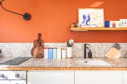 - un comptoir de cuisine avec un évier et un mur orange dans l'établissement Charming Apartment - Montmartre - 4 guests, à Paris