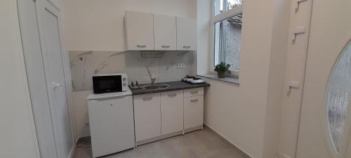 a small kitchen with white cabinets and a microwave at Déri Kert Apartmanház B in Baja
