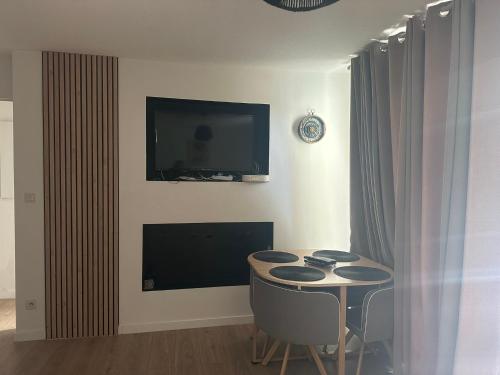 a living room with a table and a tv on the wall at Appartement cosy avec balcon et piscine in Besançon