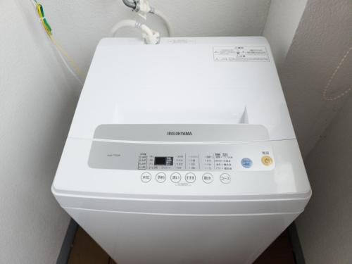 a white washing machine in a corner of a room at アワセベイストリートホテル in Okinawa City