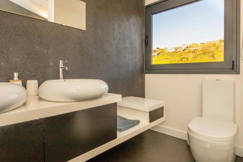 un bagno con lavandino, WC e finestra di Villa Leonor Cliffside Retreat a Calheta