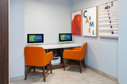 two computers on a desk with two orange chairs at Holiday Inn Express & Suites Carmel North – Westfield by IHG in Carmel