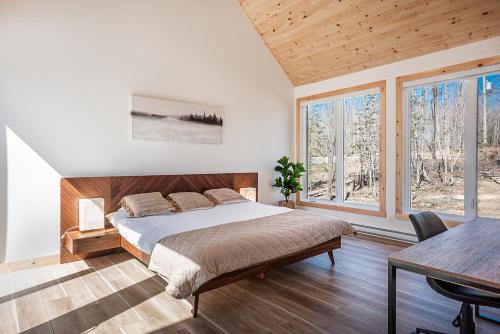 a bedroom with a bed and a table and windows at Lilia Chalet Urbain de Luxe près du Mont-Tremblant in Saint-Rémi-dʼAmherst