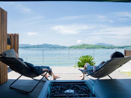 two people sitting in chairs on a patio with a view of the water at Rakuten STAY HOUSE Amakusa 105 pet allowed in Kami Amakusa