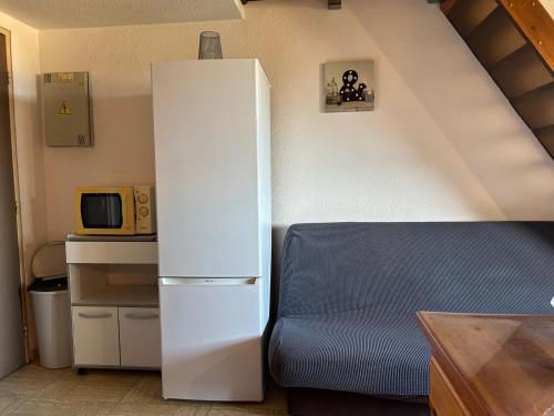 Cette chambre comprend un réfrigérateur blanc et un canapé bleu. dans l'établissement T2 Mezzanine Saint-Cyprien: Proche Plage, Parking Sécurisé, Équipé, Animaux Acceptés - FR-1-793-6, à Saint-Cyprien