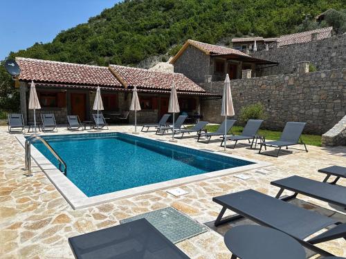 a swimming pool with chairs and umbrellas next to a house at Eco Villas Merak in Virpazar