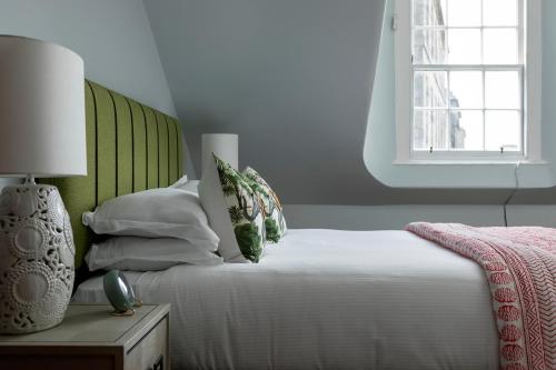 a white bed with a green headboard and a window at The Broughton Townhouse in Edinburgh