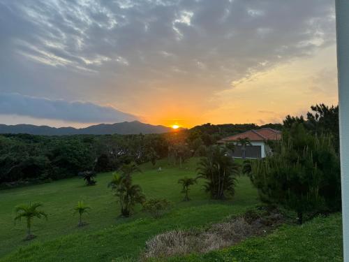 a sunset over a field with a house and palm trees at Beachfront Paradise Ishigaki in Ishigaki Island