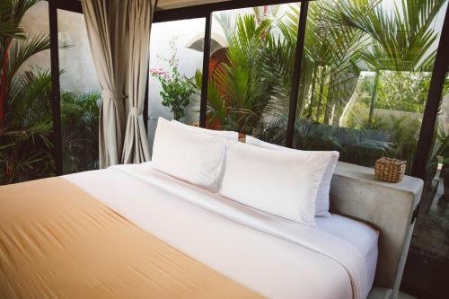 a bed with white pillows in a room with palm trees at SIVANA, Hotel Boutique with ocean or garden views - Adults only in Uluwatu
