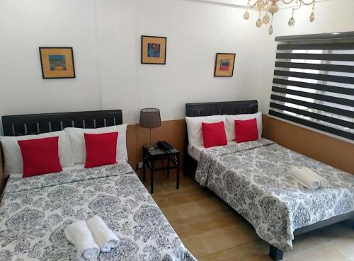 two beds in a bedroom with red and white pillows at Jil's Apartelle in Tagaytay