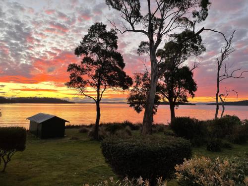 a cabin on the shore of a lake at sunset at Abs by the Bay in Taranna
