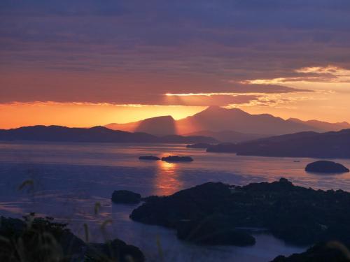 a sunset over a body of water with mountains at Flat Glamping Nagasaki in Nagasaki