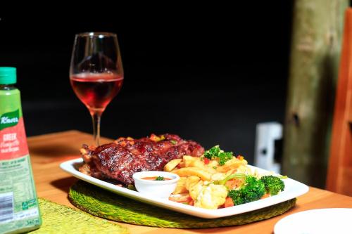 a plate of food next to a glass of wine at Olive Country Lodge - Eswatini in Ngwempisi