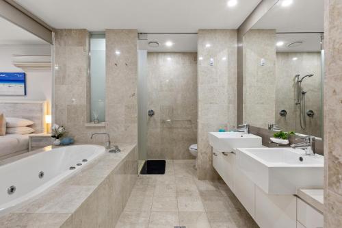 ein Badezimmer mit zwei Waschbecken, einer Badewanne und einer Dusche in der Unterkunft Luxe King Studio Apartment in Santai Resort in Casuarina
