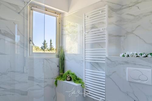 La salle de bains est pourvue de murs en marbre blanc et d'une fenêtre. dans l'établissement Montfleuri, à Villeneuve-Loubet