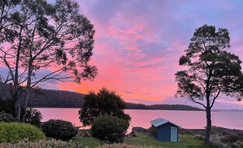 a shed on the shore of a lake at sunset at Abs by the Bay in Taranna