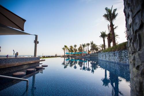 a swimming pool next to a beach with palm trees at JA Palm Tree Court, Dubai in Dubai