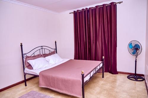 1 dormitorio con 1 cama con cortinas rojas y ventilador en Mount Meru View Homestay, en Arusha