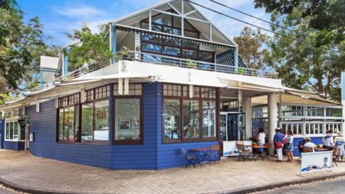 a blue building with people standing outside of it at Sand & Sea - Pearl Beach With Pool in Pearl Beach