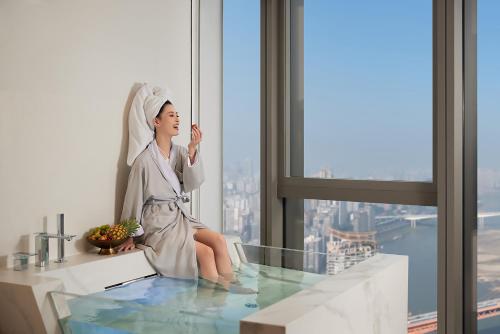 a woman sitting in a bath tub in a room with a window at ISEYA Panoramic Hotel Chongqing Jiefangbei Raffles Plaza in Chongqing