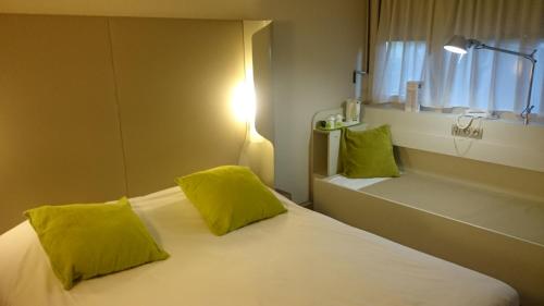 Un dormitorio con una cama con almohadas amarillas y una ventana en Campanile Bayonne, en Bayona