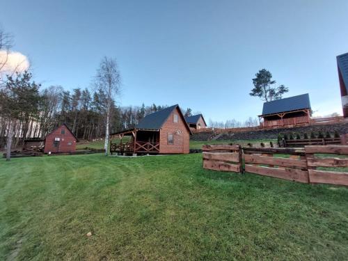a field with a wooden fence and some barns at Kaszubskie Domki Nad Jeziorem Bluj in Głodowo
