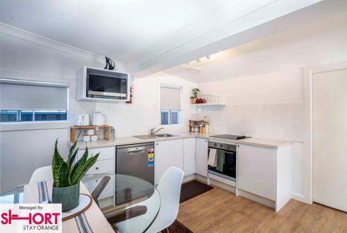 a kitchen with white cabinets and a glass table at Bright, Cosy Cottage near CBD- Free wifi, Netflix and Disney Plus in Orange