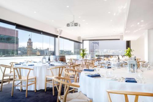 a restaurant with white tables and chairs and large windows at Rydges Sydney Central in Sydney