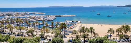 a beach with a marina with boats and palm trees at Hotel Espadon bleu in Le Lavandou