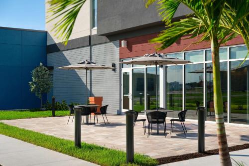 a group of tables and chairs with umbrellas in front of a building at Hyatt Place Melbourne Airport, Fl in Melbourne