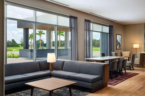 a living room with a couch and tables and windows at Hyatt Place Melbourne Airport, Fl in Melbourne