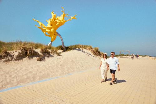 a man and woman walking on the beach with a kite at Holiday Suites Westende - Middelkerke in Middelkerke